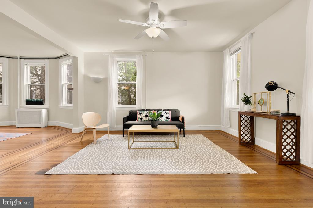 Furnished living room with hardwood floors, a patterned rug, black sofa, and tall windows.