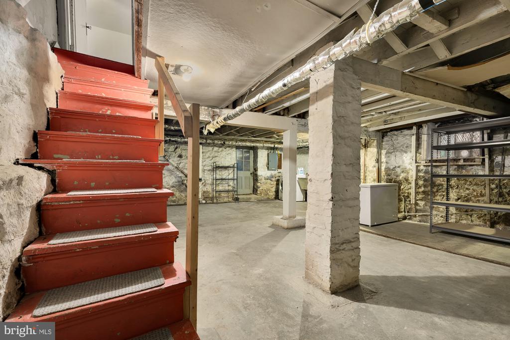 Unfinished basement with red stairs, exposed stone walls, and metal shelving.