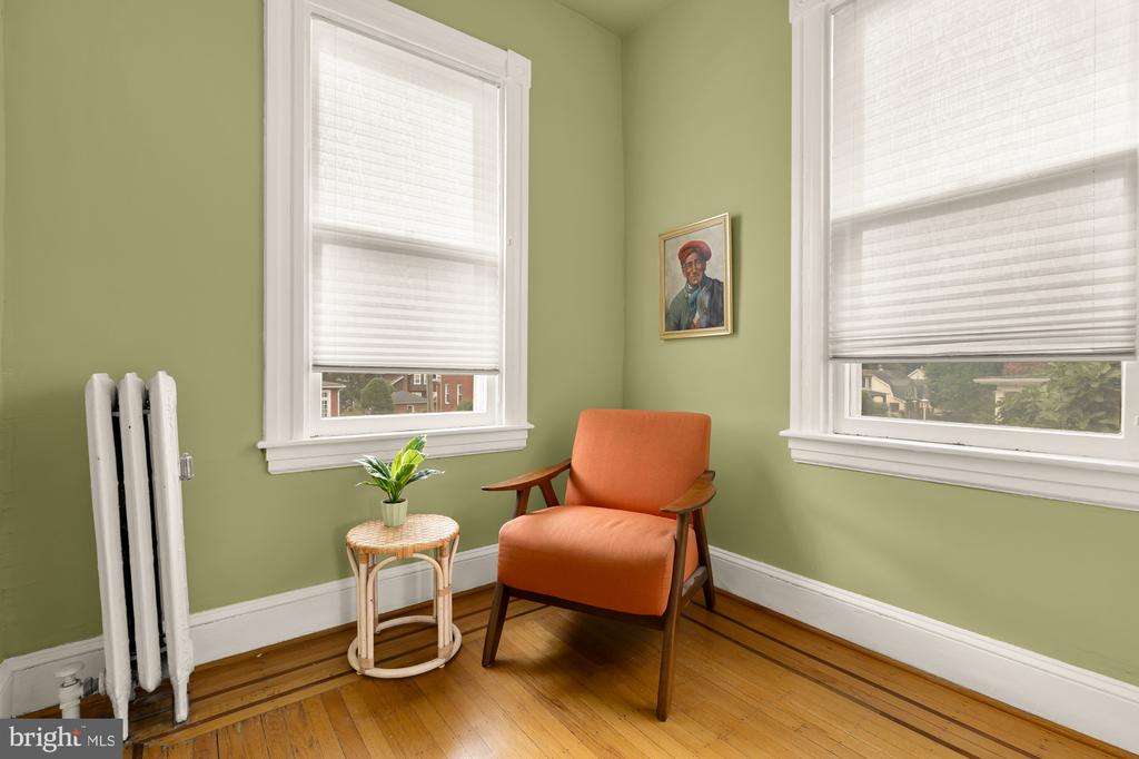Sitting area with an orange armchair, sage-green walls, tall shaded windows, and hardwood floors.