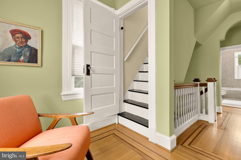 Entryway with an open door to black-and-white stairs, hardwood floors, and an orange chair.