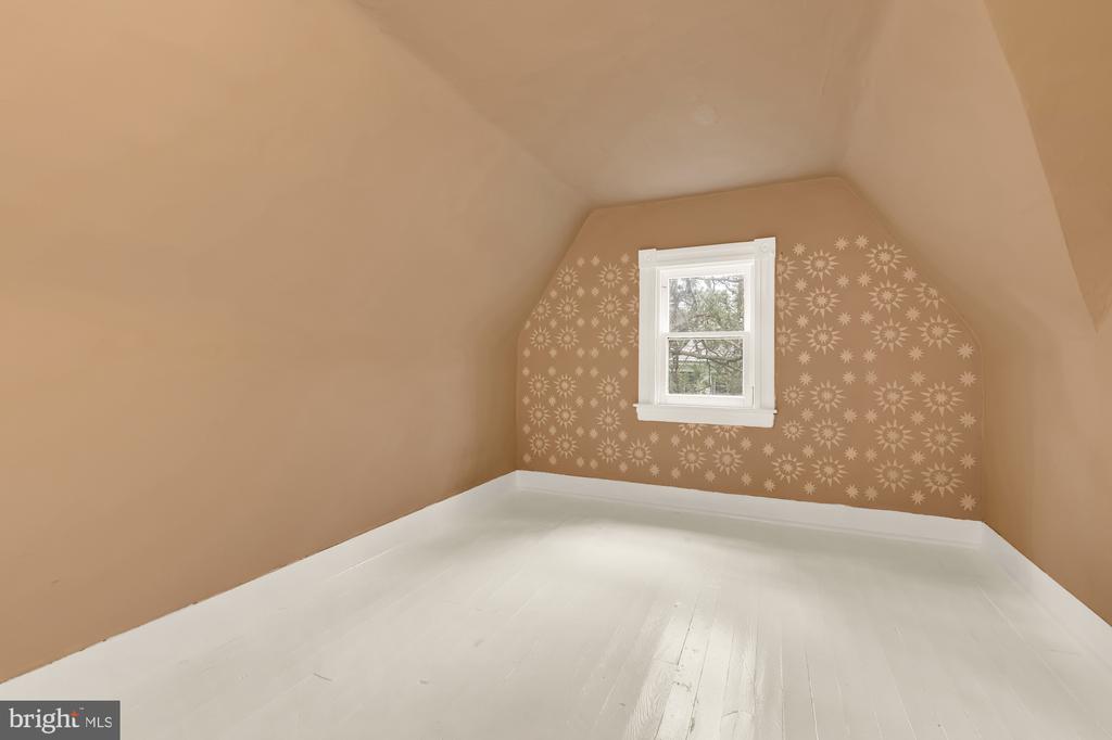 Empty attic room with white flooring, sloped walls, and a patterned wall around the window.