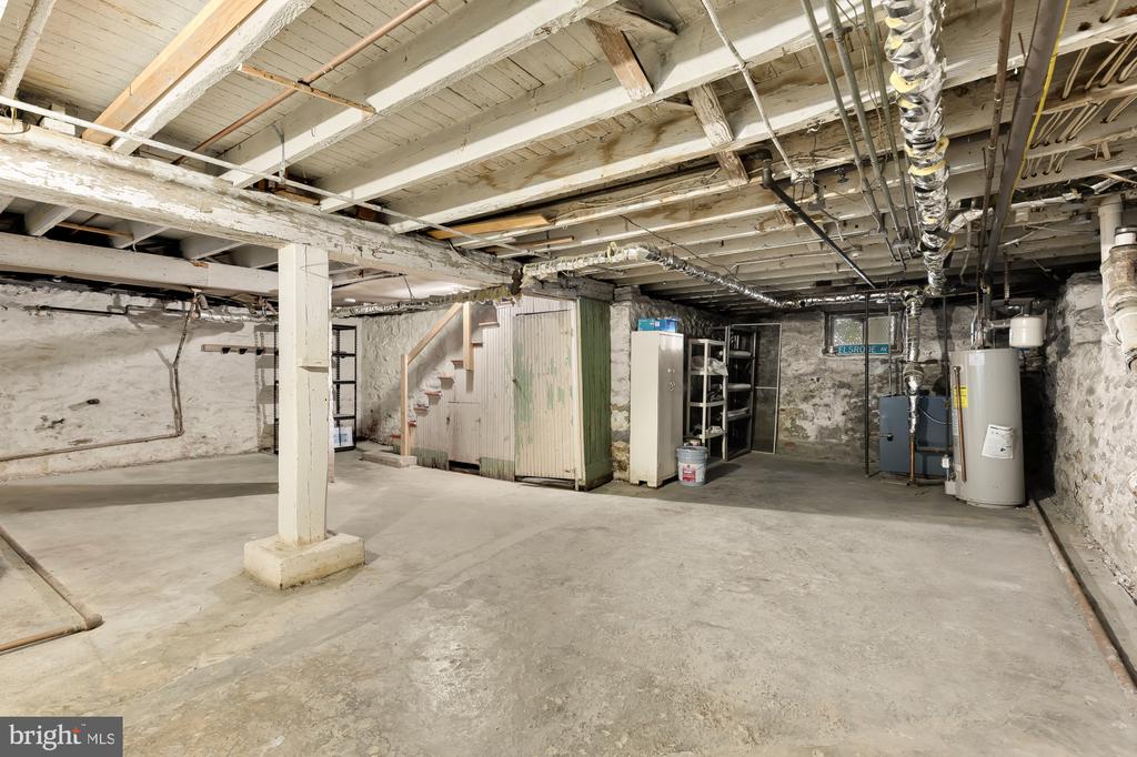 Unfinished basement with exposed ceiling joists, stone walls, and utility equipment.
