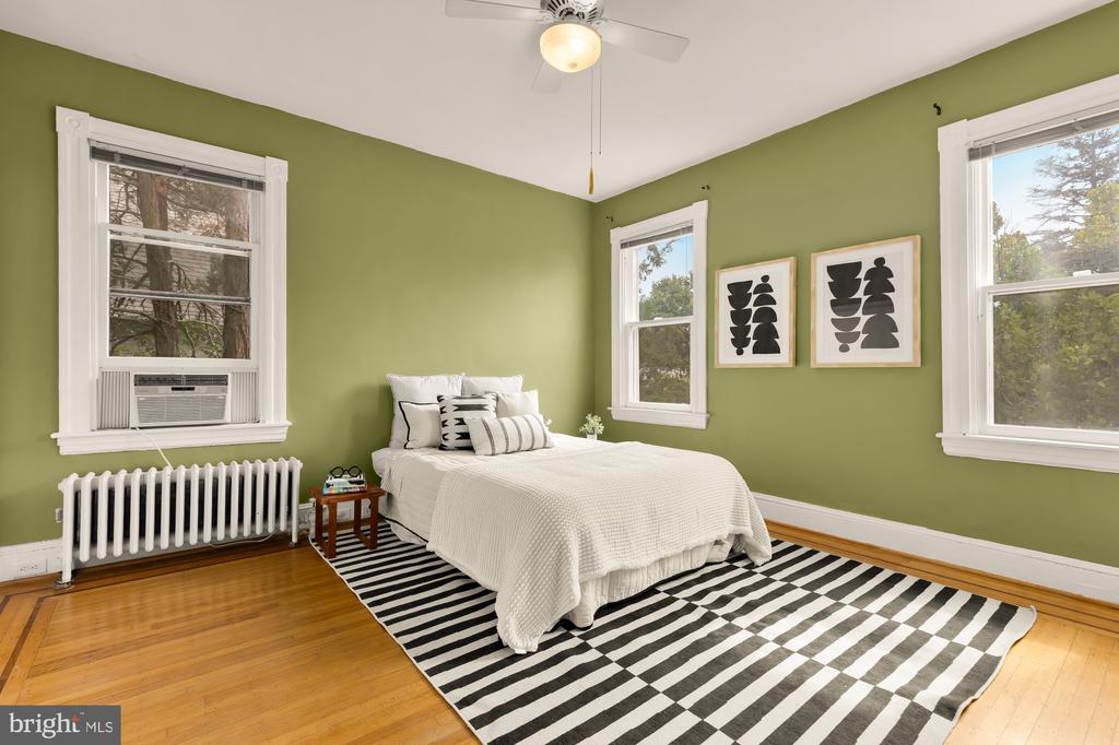 Bedroom with olive-green walls, a white bed, striped rug, and three windows.