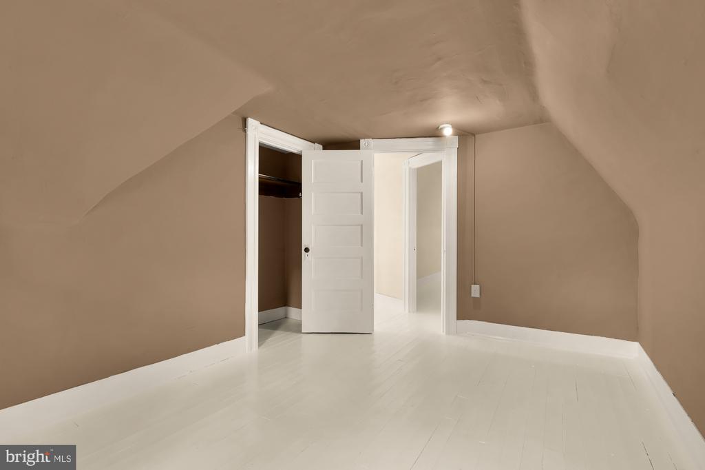 Empty attic room with a low sloped ceiling, white flooring, and an open closet.