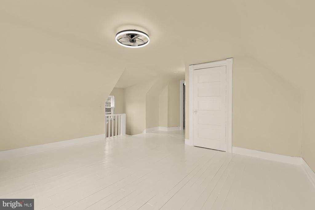 Vacant finished attic with white plank flooring, sloped walls, a paneled door, and ceiling fan.