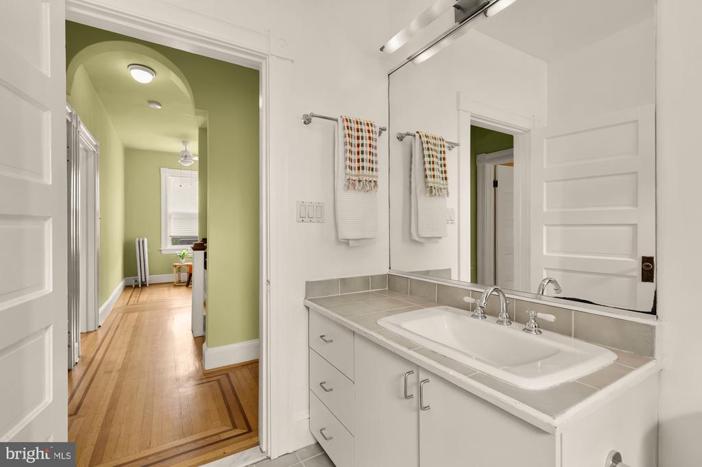 Bathroom vanity with a large mirror and patterned towels beside a green hallway.