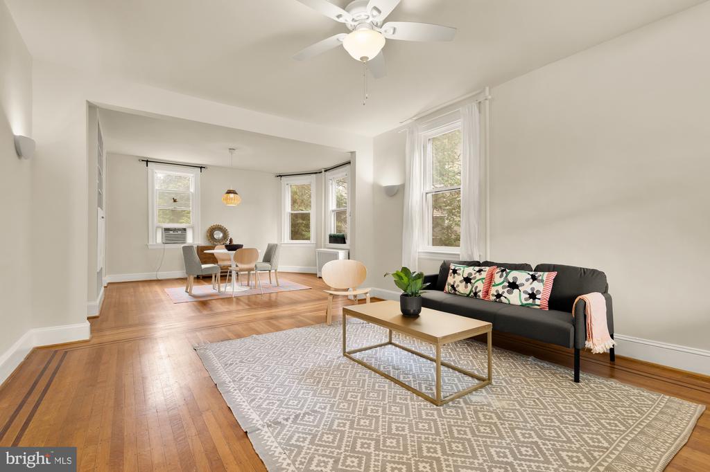Living room with hardwood floors, a dark sofa, and an adjoining dining area by tall windows.