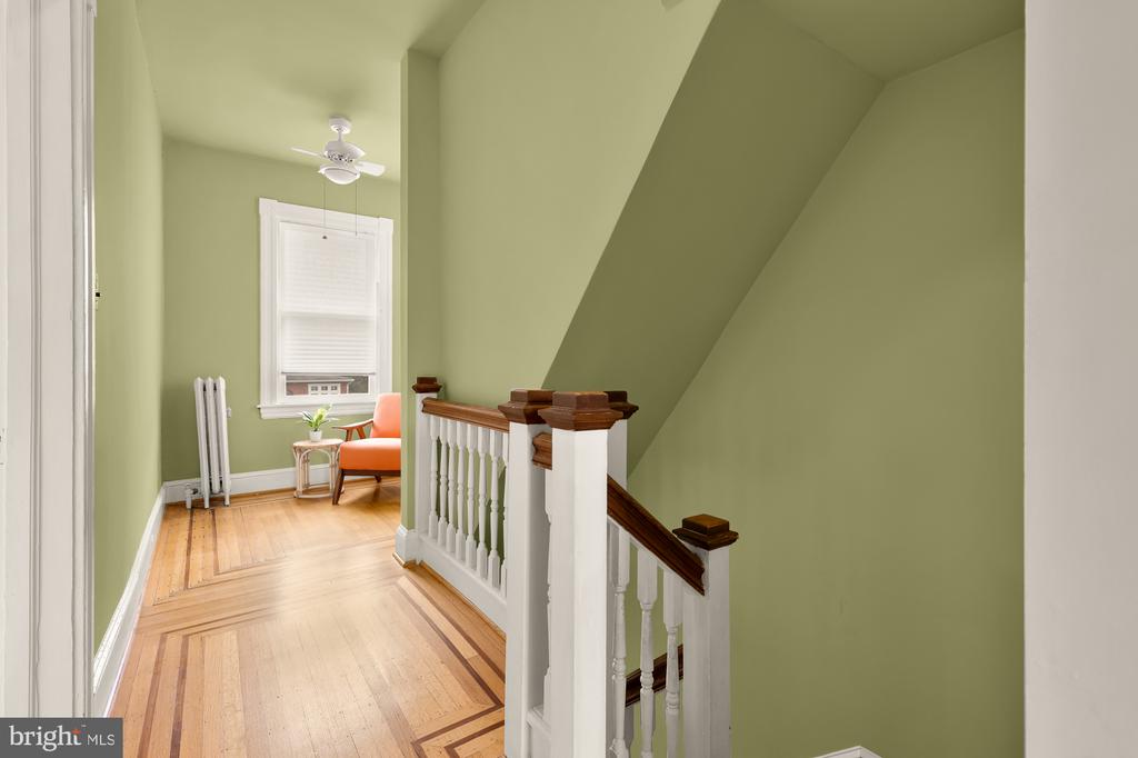 Upstairs landing with green walls, patterned wood floors, white balustrade, and a small sitting nook.