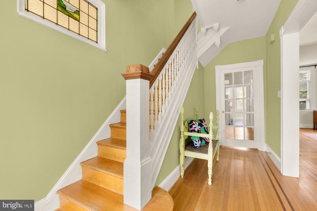 Foyer with a wooden staircase, stained-glass window, hardwood floors, and a small chair.
