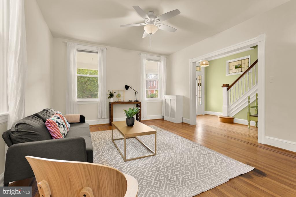 Living room with hardwood floors, patterned rug, gray sofa, and staircase opening.