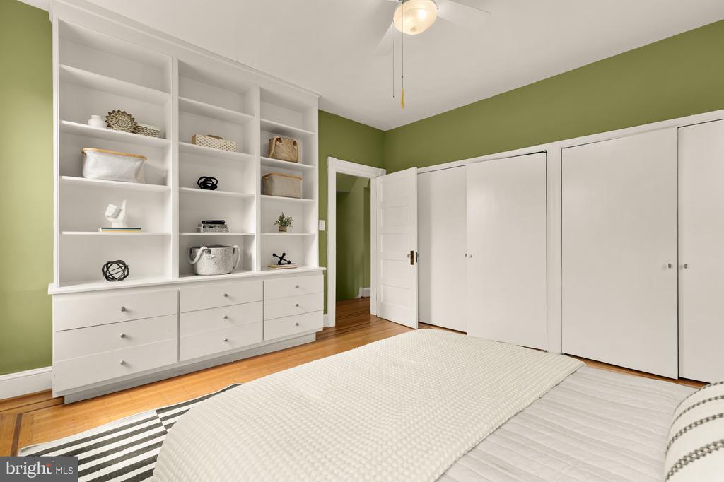 Bedroom with olive-green walls, built-in white shelving, large closets, and a bed with a cream coverlet.