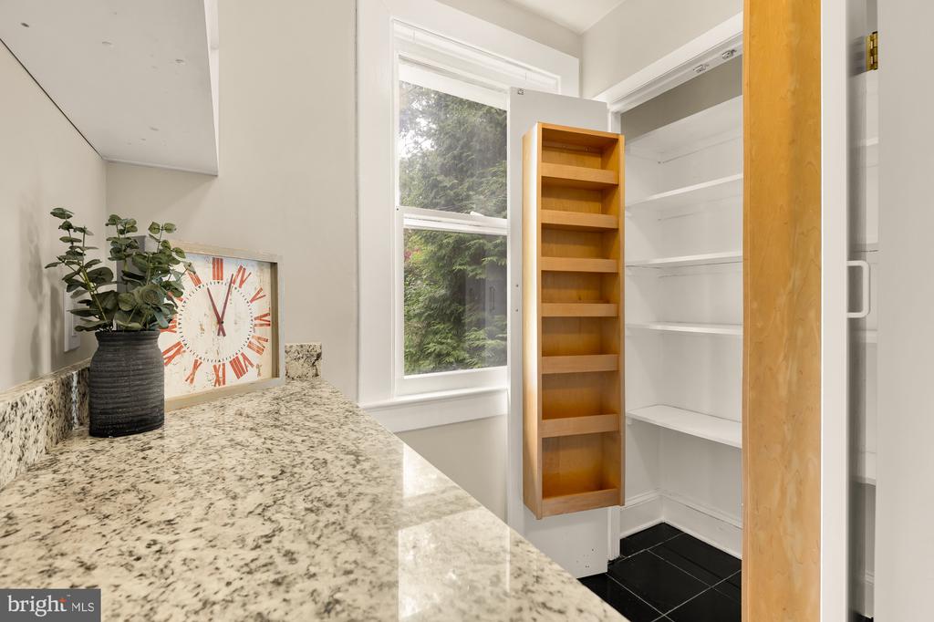 Kitchen pantry with open white shelves, a wooden pull-out rack, and a granite countertop.