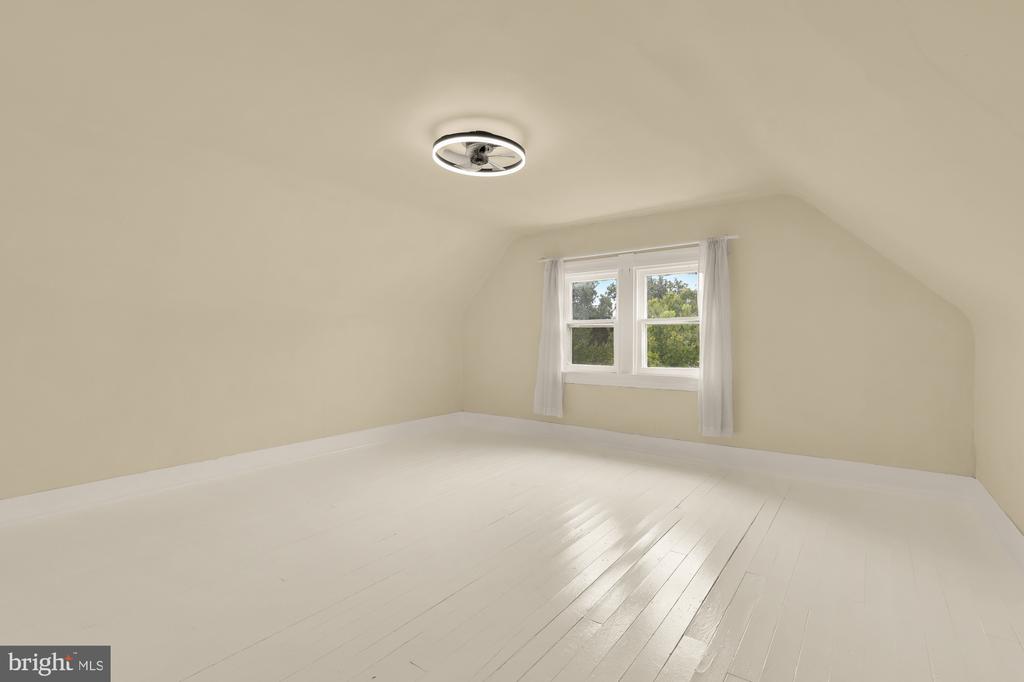 Empty upper-floor room with white plank floors, sloped ceiling, and two curtained windows.