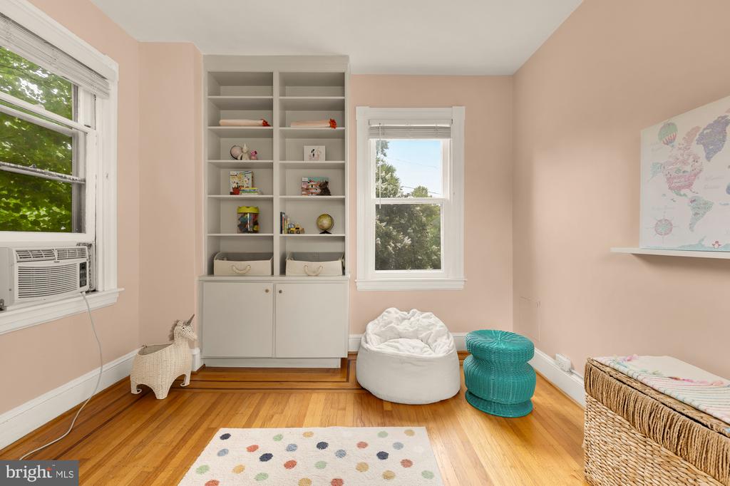 Child’s playroom with built-in shelving, peach walls, hardwood floors, and colorful seating.
