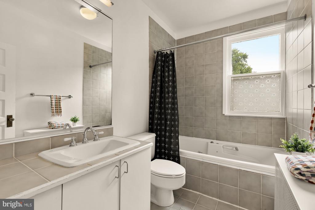 Bathroom with tiled bathtub, black patterned shower curtain, and wide vanity mirror.