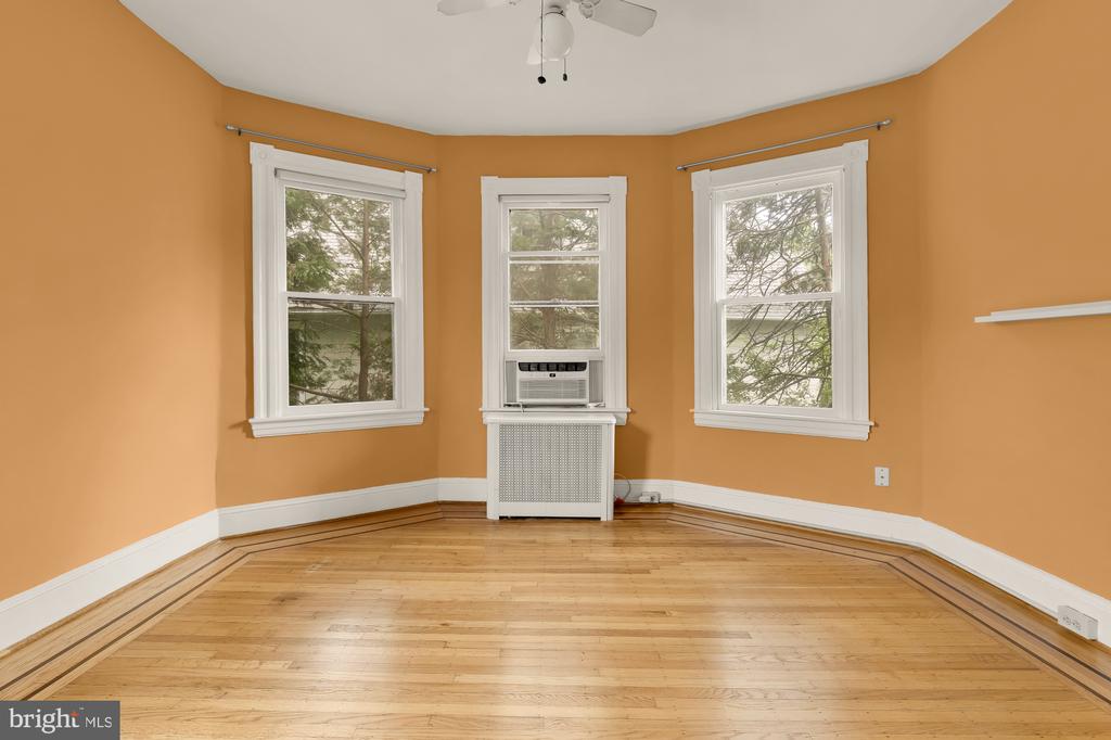 Empty room with orange walls, three windows, a window air conditioner, and inlaid hardwood flooring.