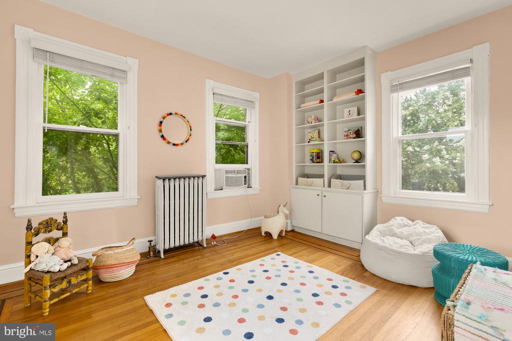 Bright peach bedroom with built-in shelving, hardwood floors, and a colorful polka-dot rug.
