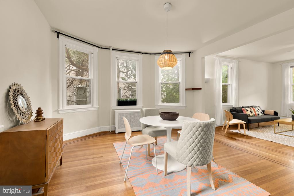 Open-plan living and dining area with bay windows, hardwood floors, and a round white table.