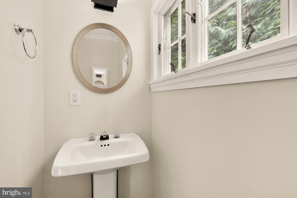 Bathroom with a white pedestal sink, round mirror, and wide window overlooking greenery.