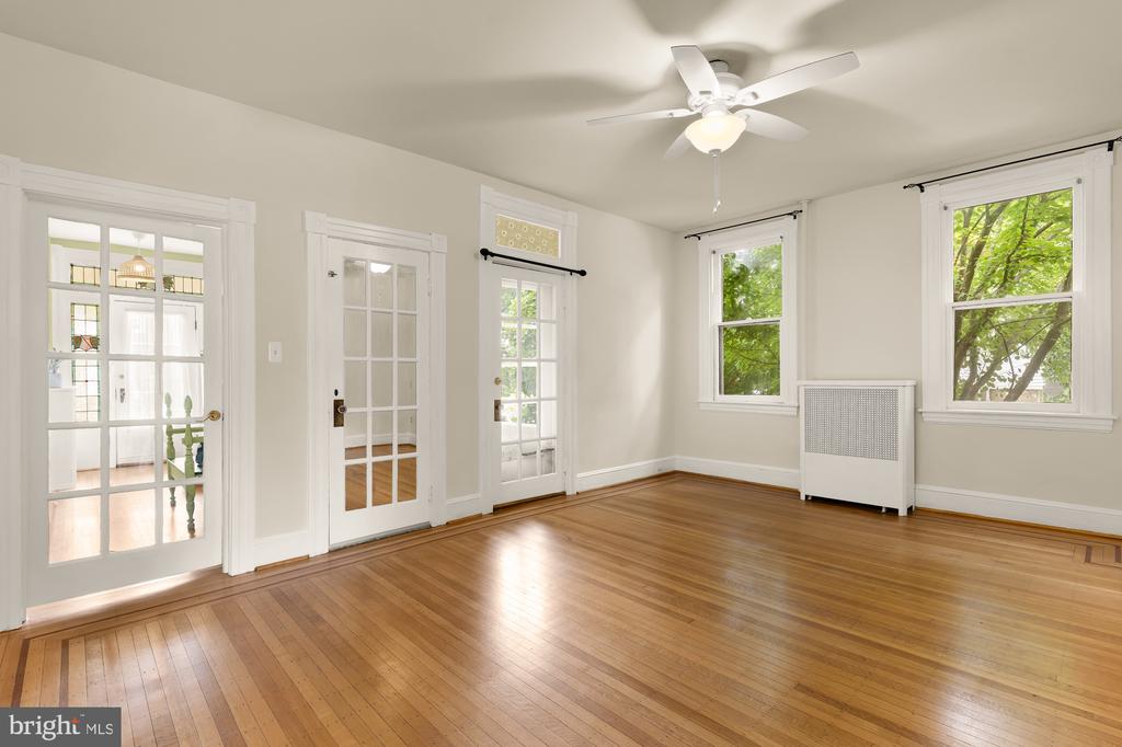Vacant room with hardwood floors, French doors, tall windows, and a ceiling fan.