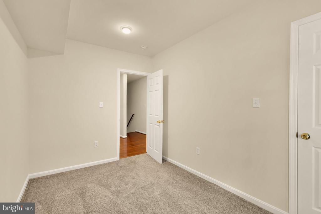 Empty carpeted room with beige walls and an open doorway to a hardwood-floored hall.
