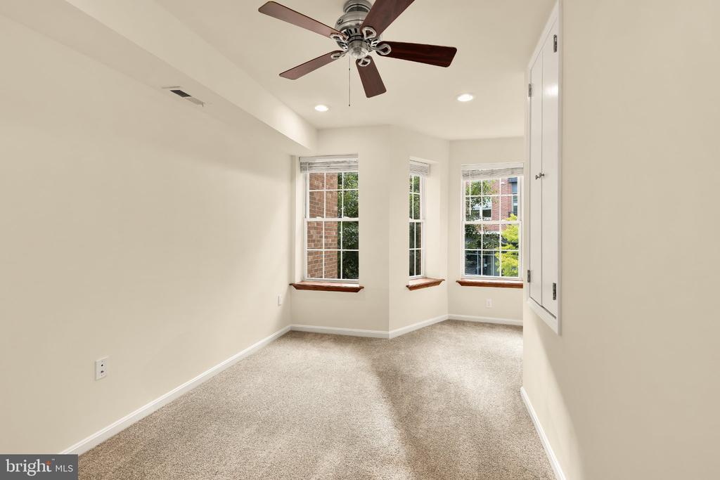Empty bedroom with beige carpet, a ceiling fan, and three tall windows.