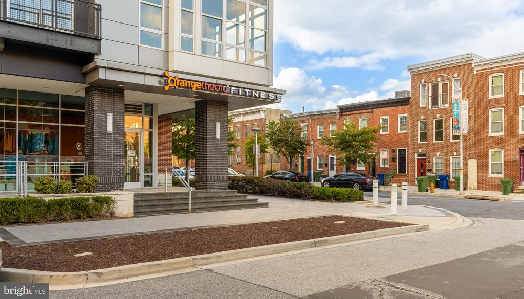 Baltimore streetscape with an Orangetheory Fitness storefront beside red-brick townhouses.