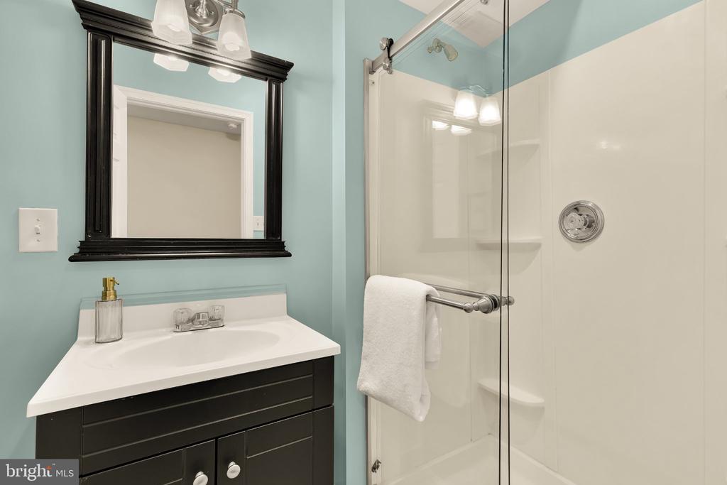 Bathroom with aqua walls, dark vanity, black-framed mirror, and glass-enclosed shower.