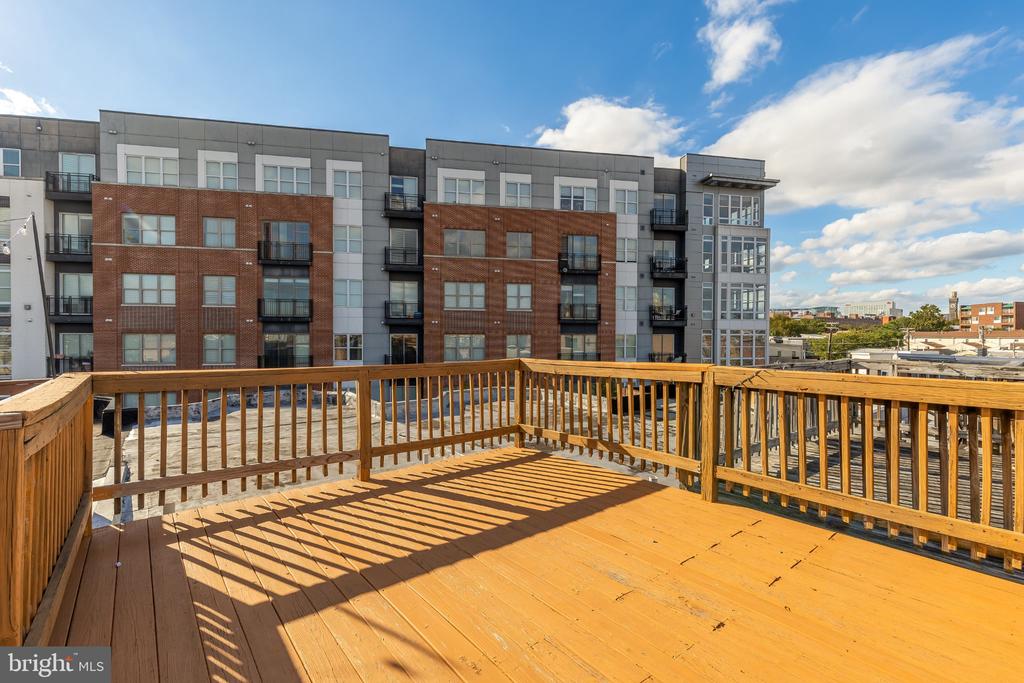 Rooftop deck with wooden railings overlooking a modern brick-and-gray apartment building.
