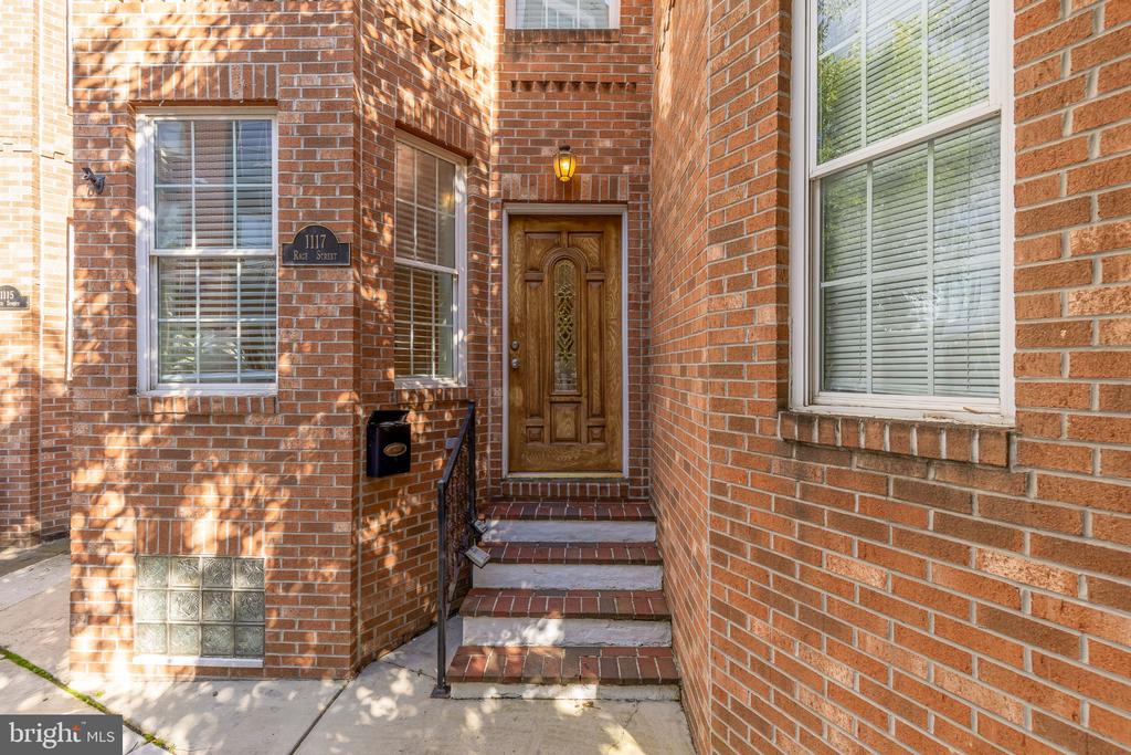 Brick home entrance with a carved wooden door, brick steps, and a 1117 Race Street plaque.