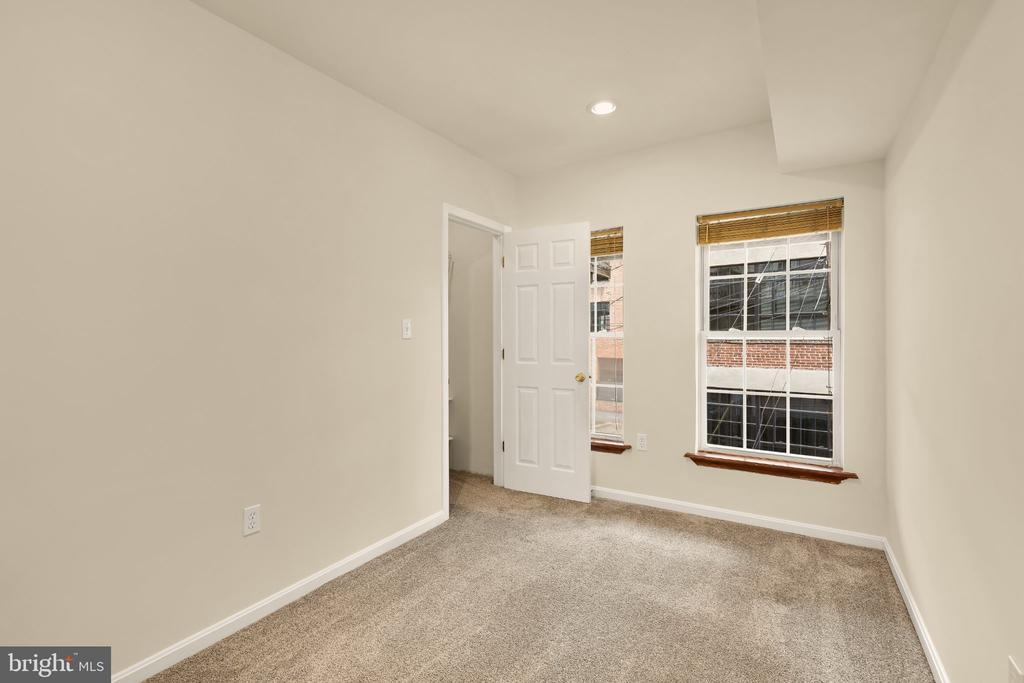 Empty bedroom with beige carpet, two windows with blinds, and an open doorway.