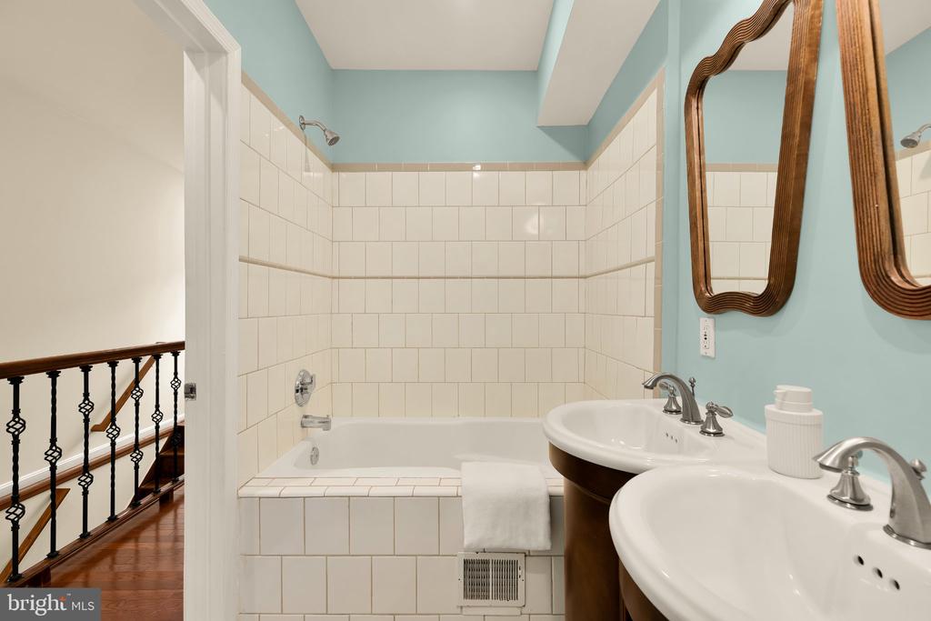 Bathroom with tiled bathtub, twin pedestal sinks, blue walls, and carved wood mirrors.