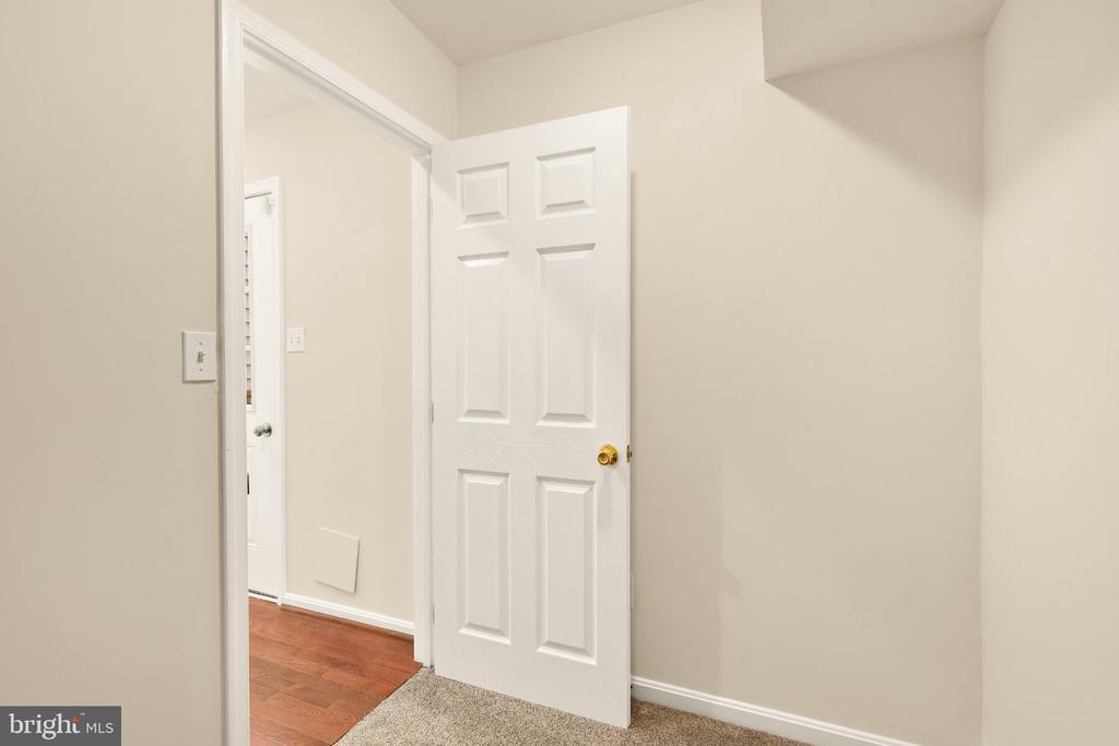 Empty carpeted room with an open paneled door leading to a hardwood-floored hallway.