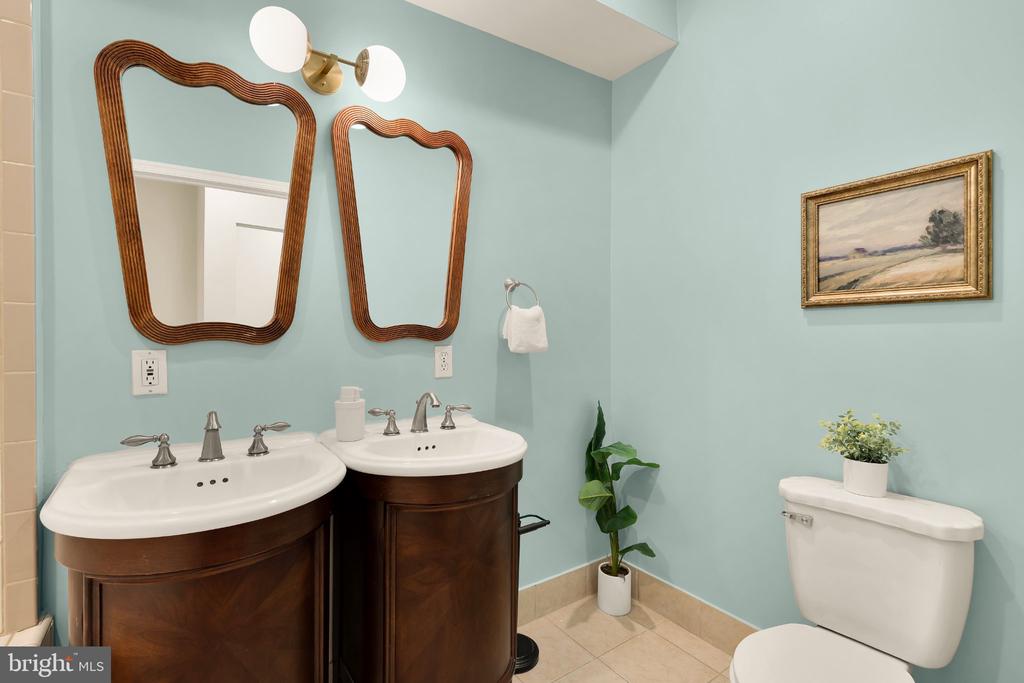 Bathroom with double dark wood vanities, wavy wood-framed mirrors, pale blue walls, and framed landscape art.