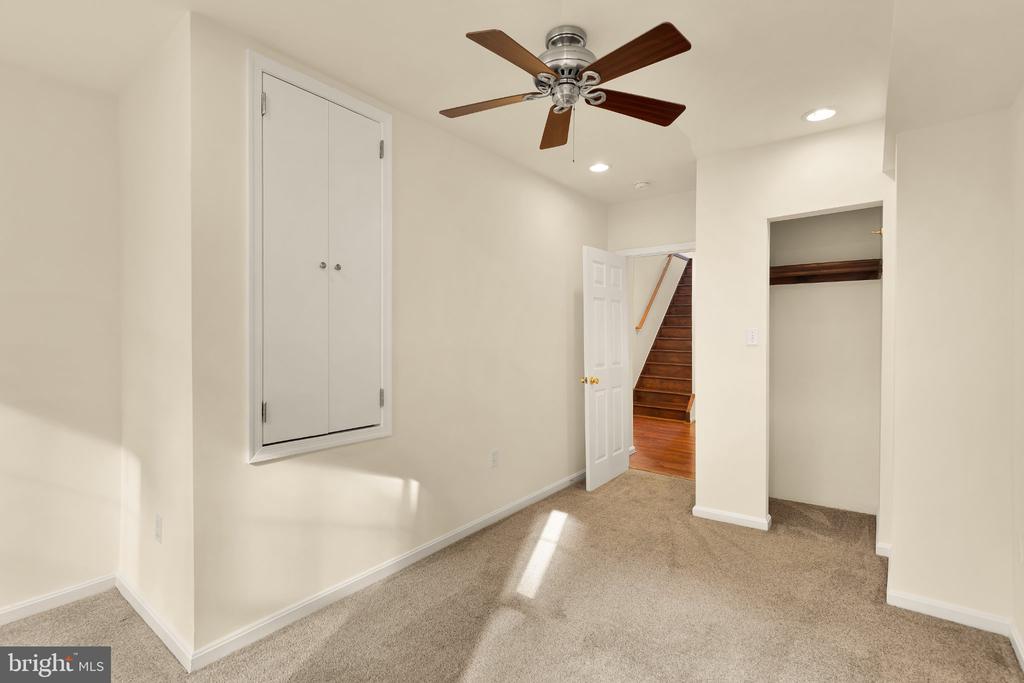 Carpeted empty room with a ceiling fan, built-in closet, and doorway to a wooden staircase.