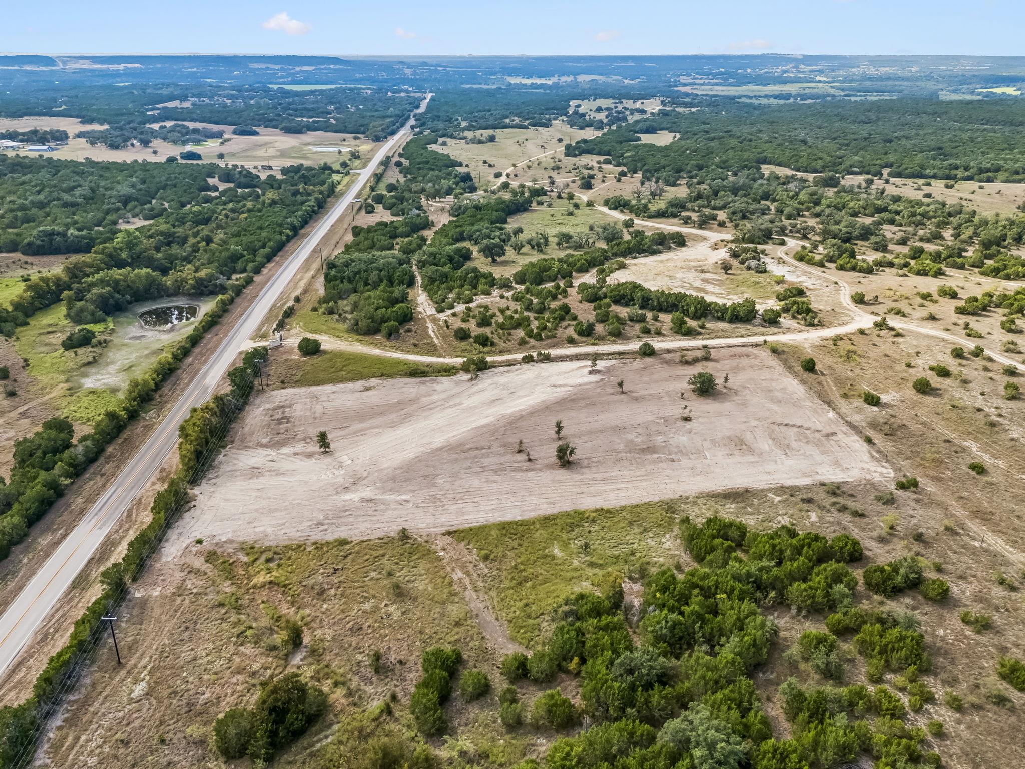 Aerial view of a cleared rural tract beside a paved road, surrounded by brush and scattered trees.