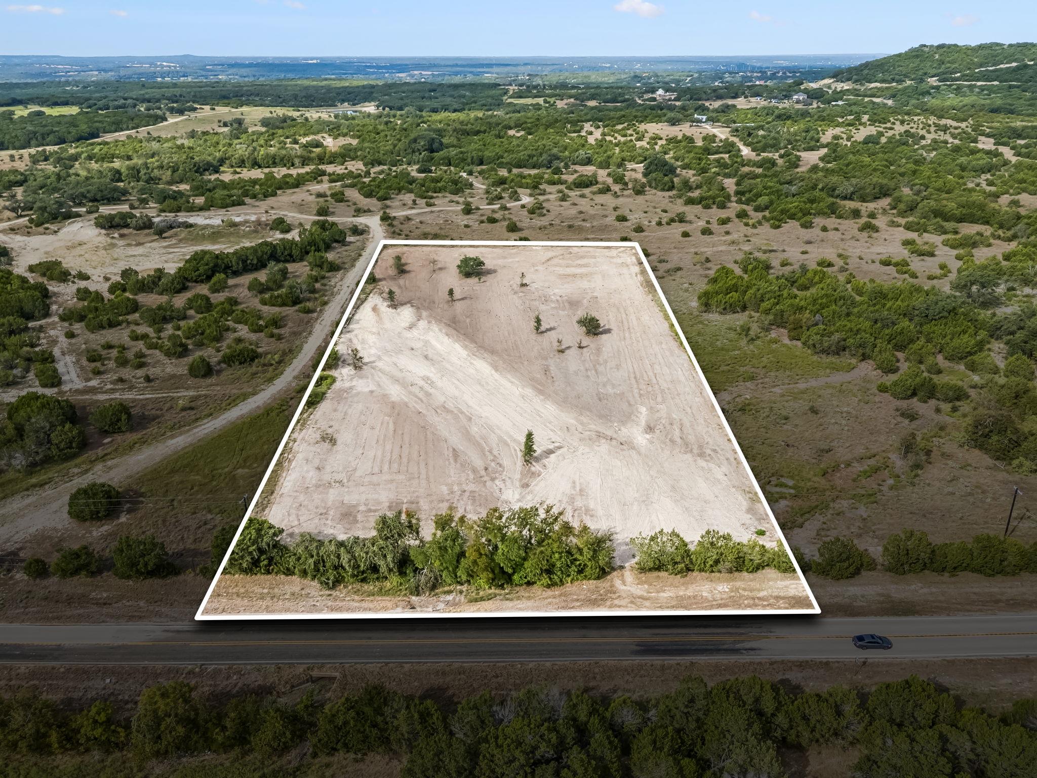 Aerial view of a cleared land parcel outlined in white, with rural scrubland and road frontage.