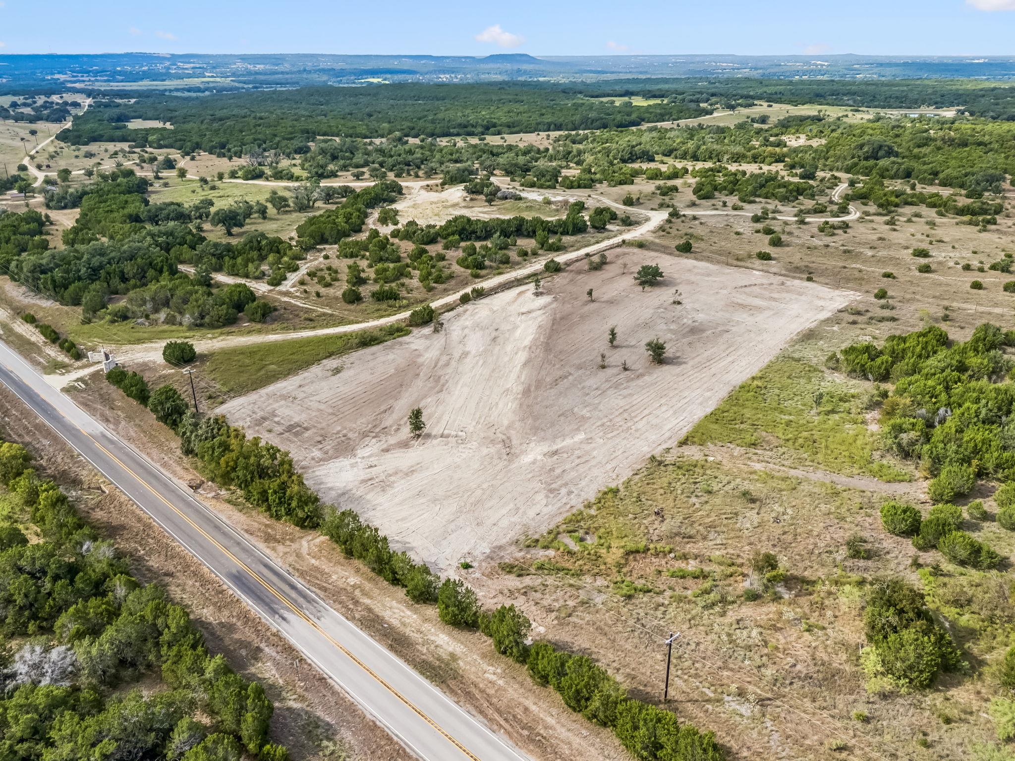 Aerial view of a cleared rural land parcel beside a paved road, surrounded by trees and scrub.
