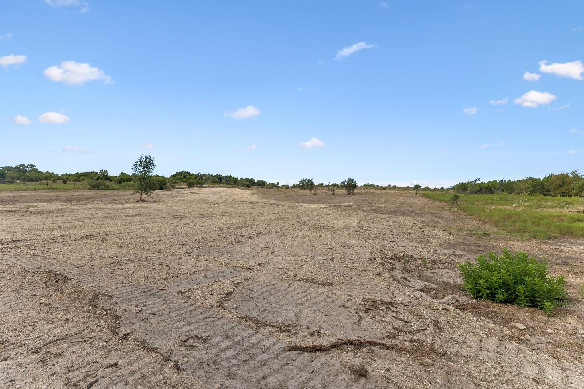 Mostly cleared dirt property with scattered trees and brush along the edges.