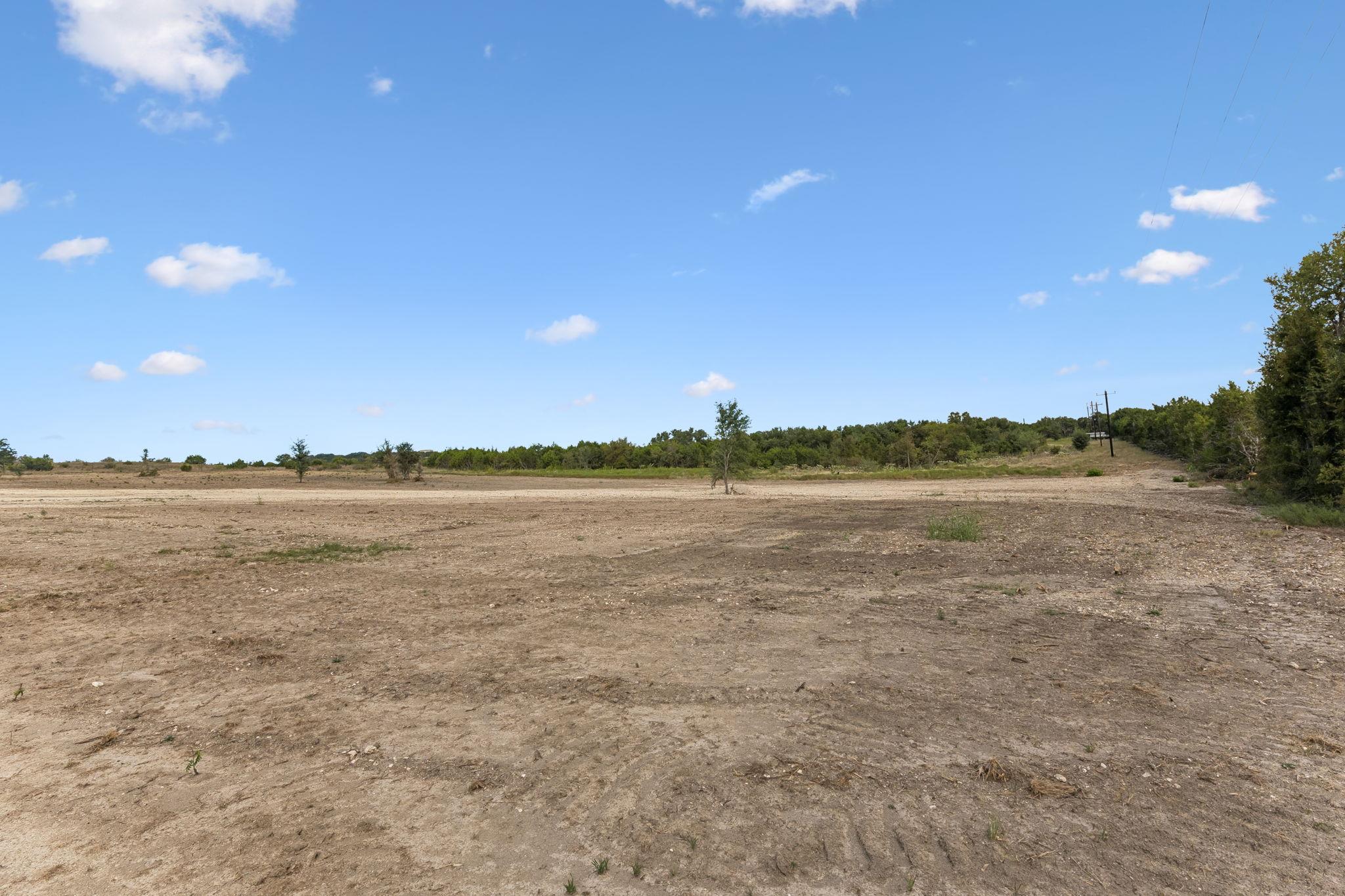 Cleared rural land with dry soil, sparse trees, and utility lines beneath a blue sky.