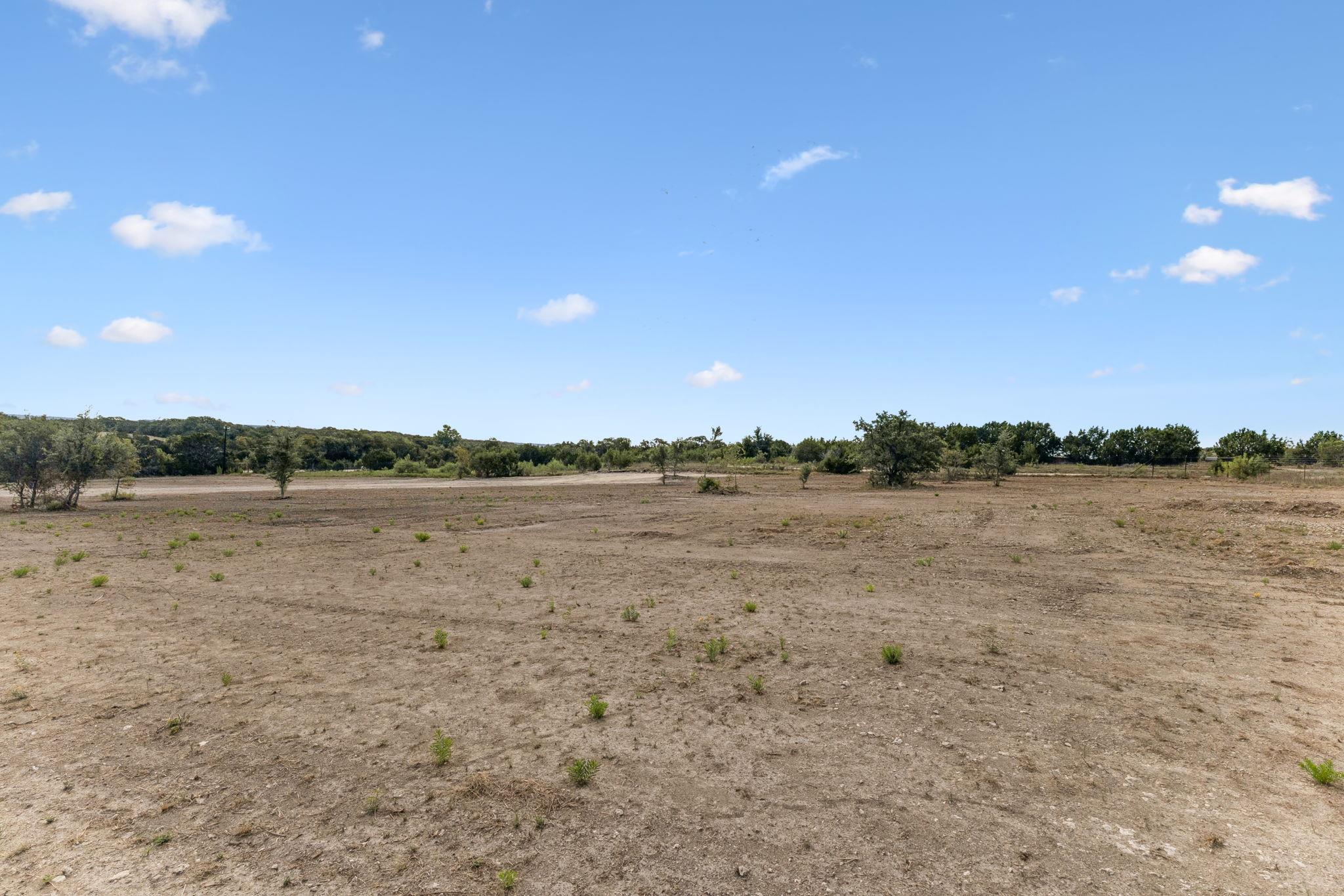 Vacant land with dry open ground, scattered shrubs, and a distant tree line.
