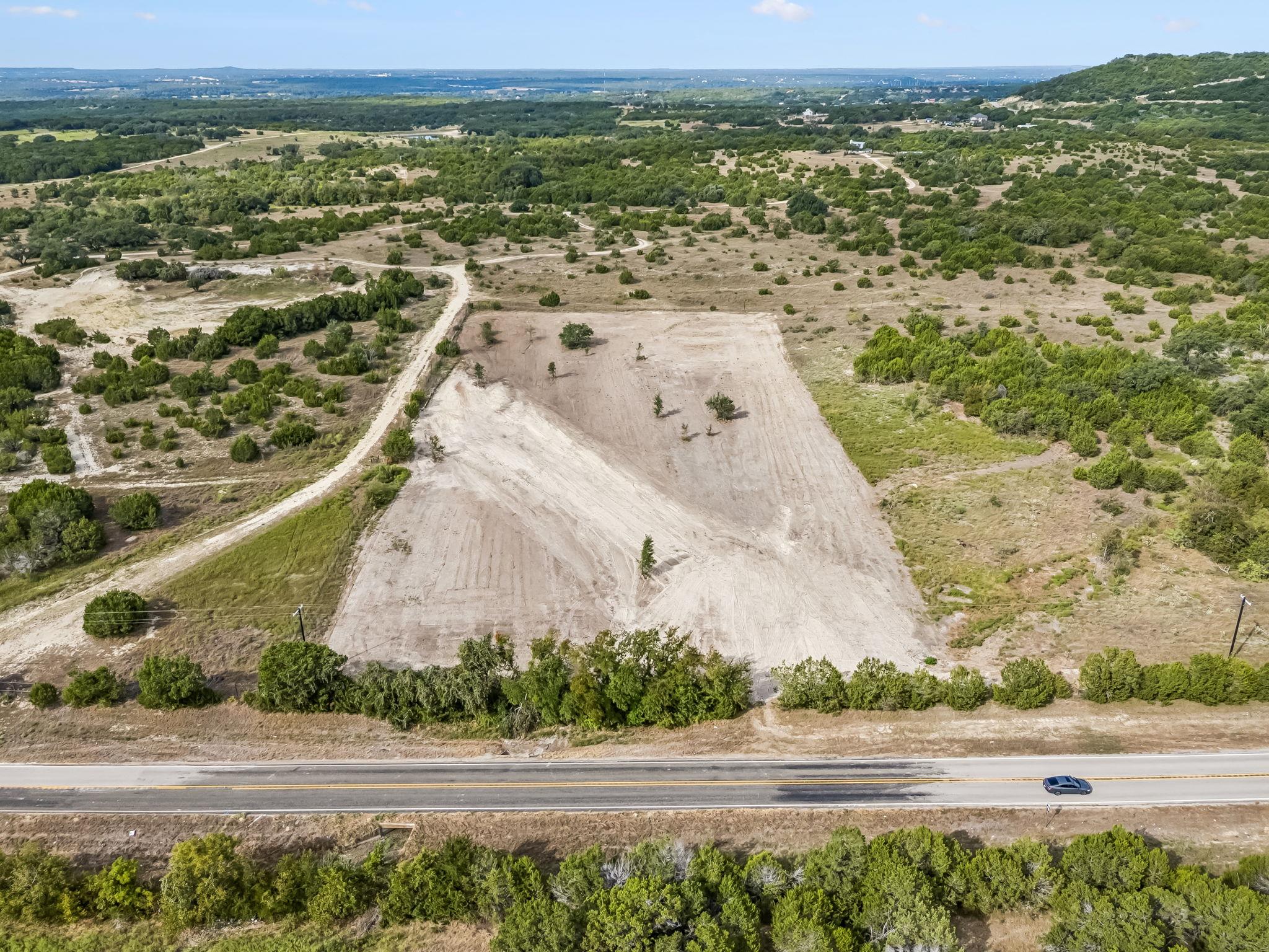 A cleared tract of land beside a highway, bordered by brush and trees.