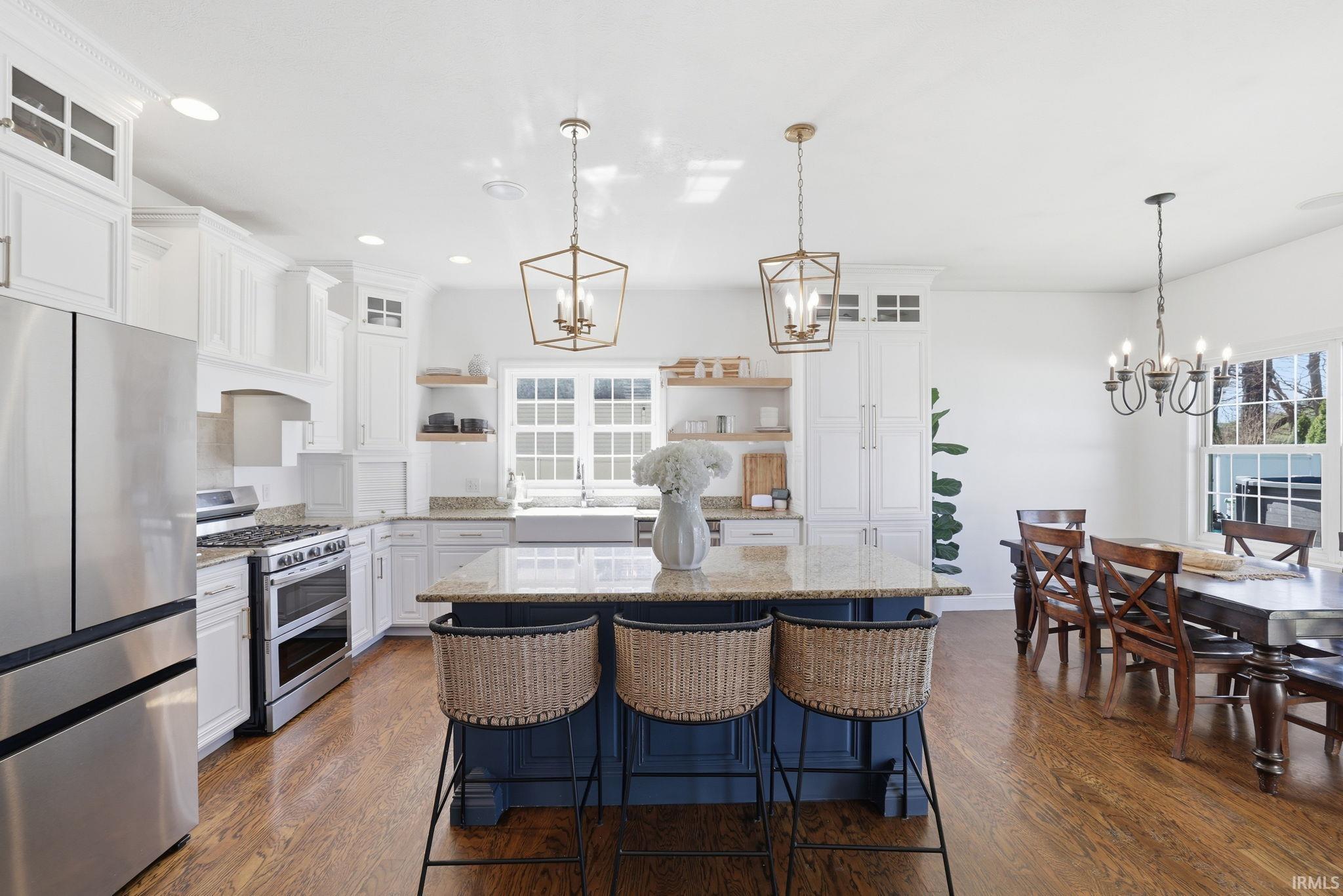 Bright kitchen with a dark blue island, woven stools, white cabinetry, and adjoining dining area.