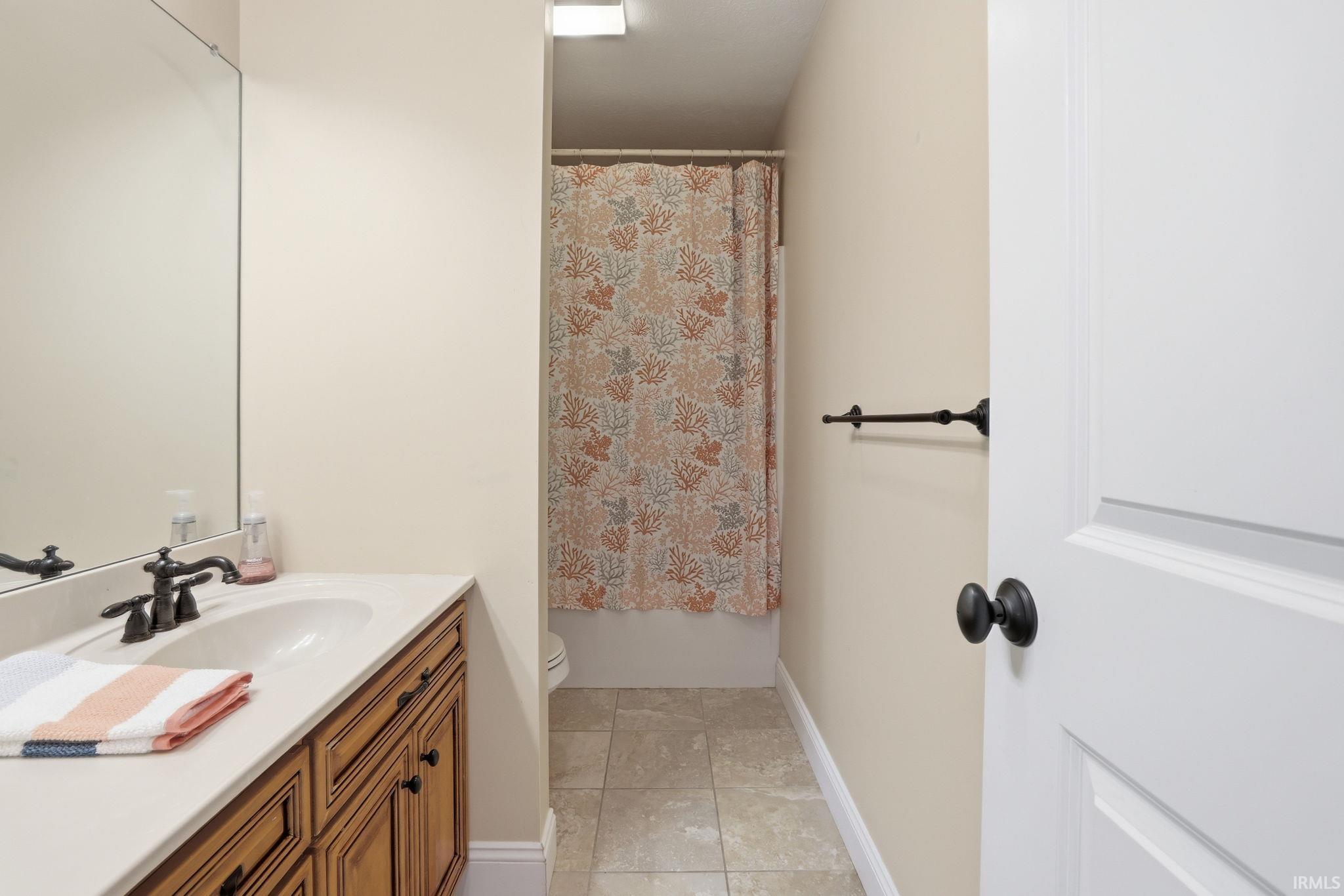 Bathroom with a wood vanity and coral-patterned shower curtain over the bathtub.