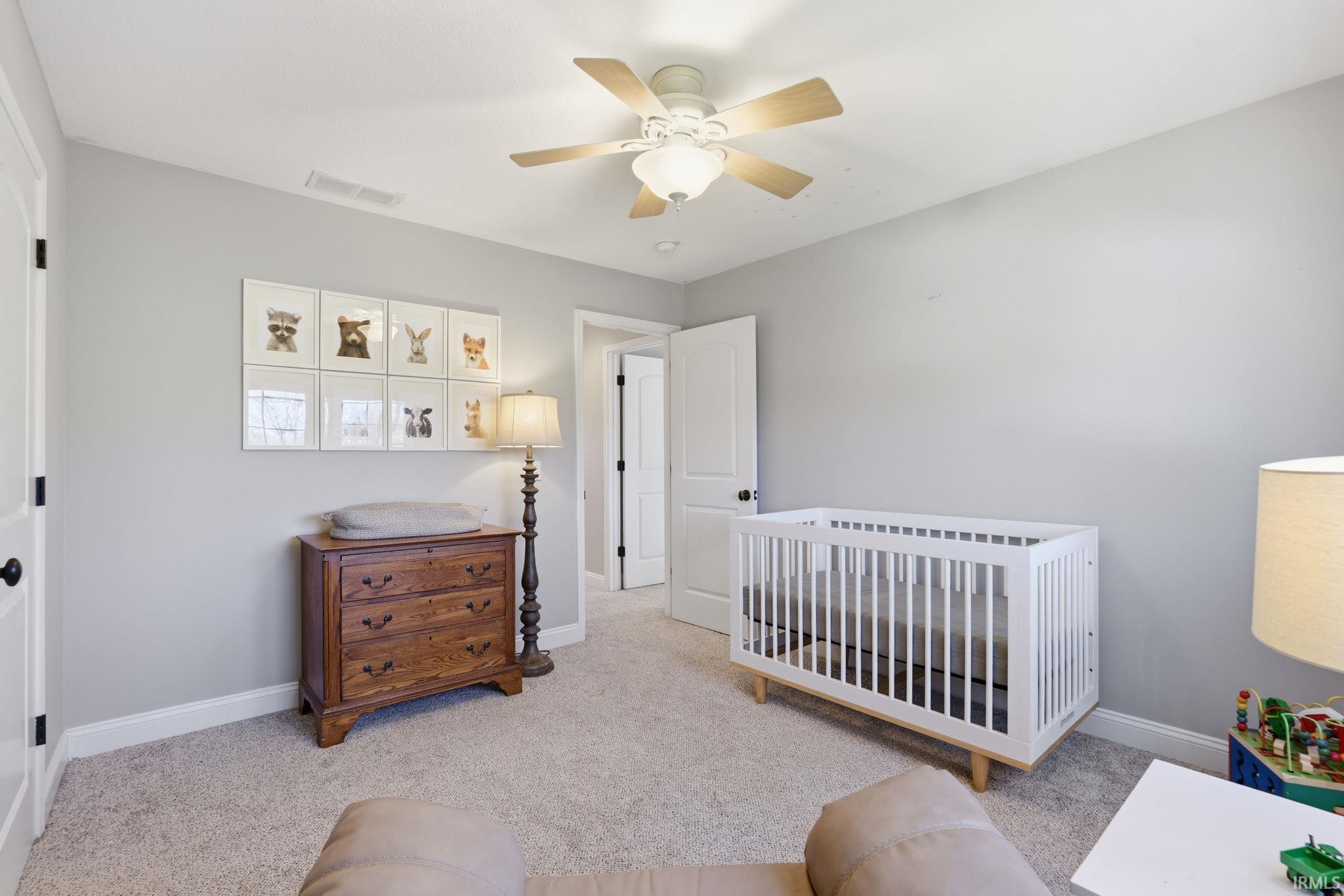 Nursery with a white crib, wooden dresser, framed animal pictures, and a ceiling fan.