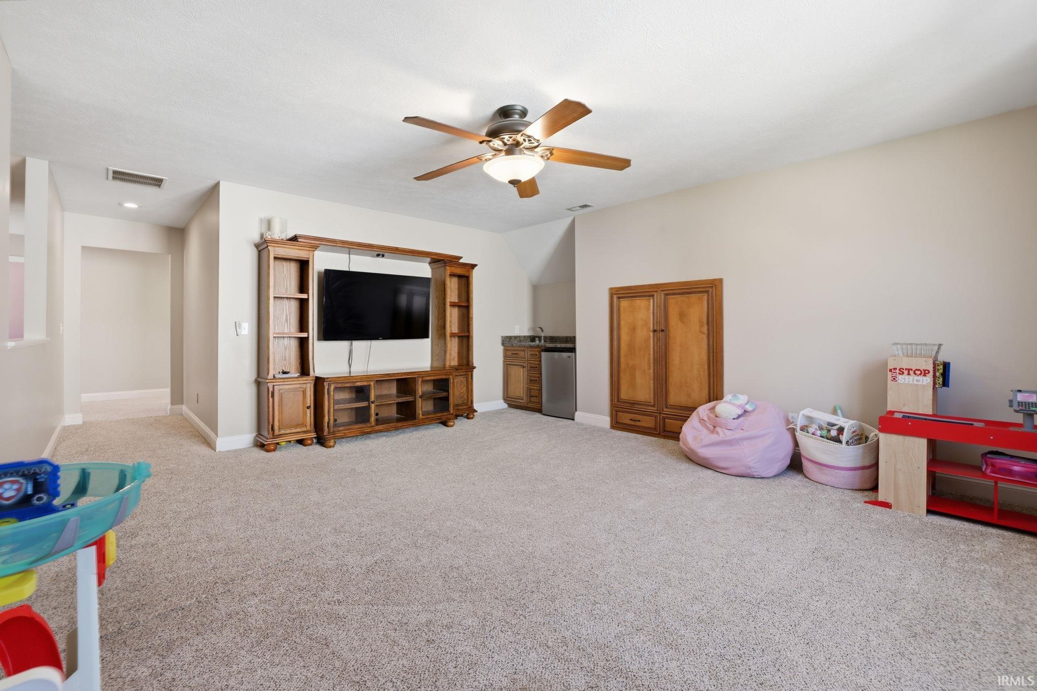 Bonus room with a wooden entertainment center, ceiling fan, small sink, and children’s play area.