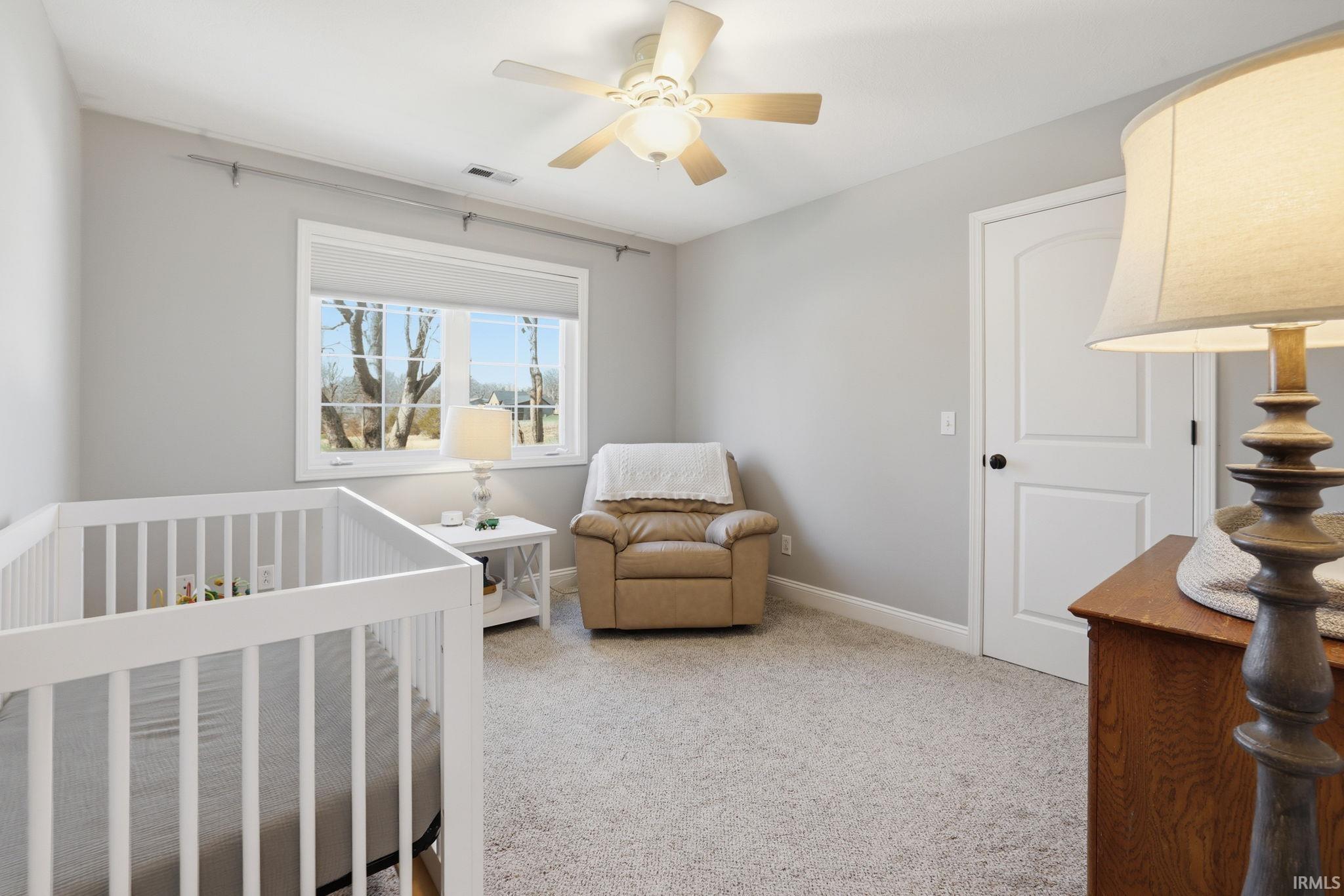 Nursery with a white crib, tan recliner, large window, and ceiling fan.