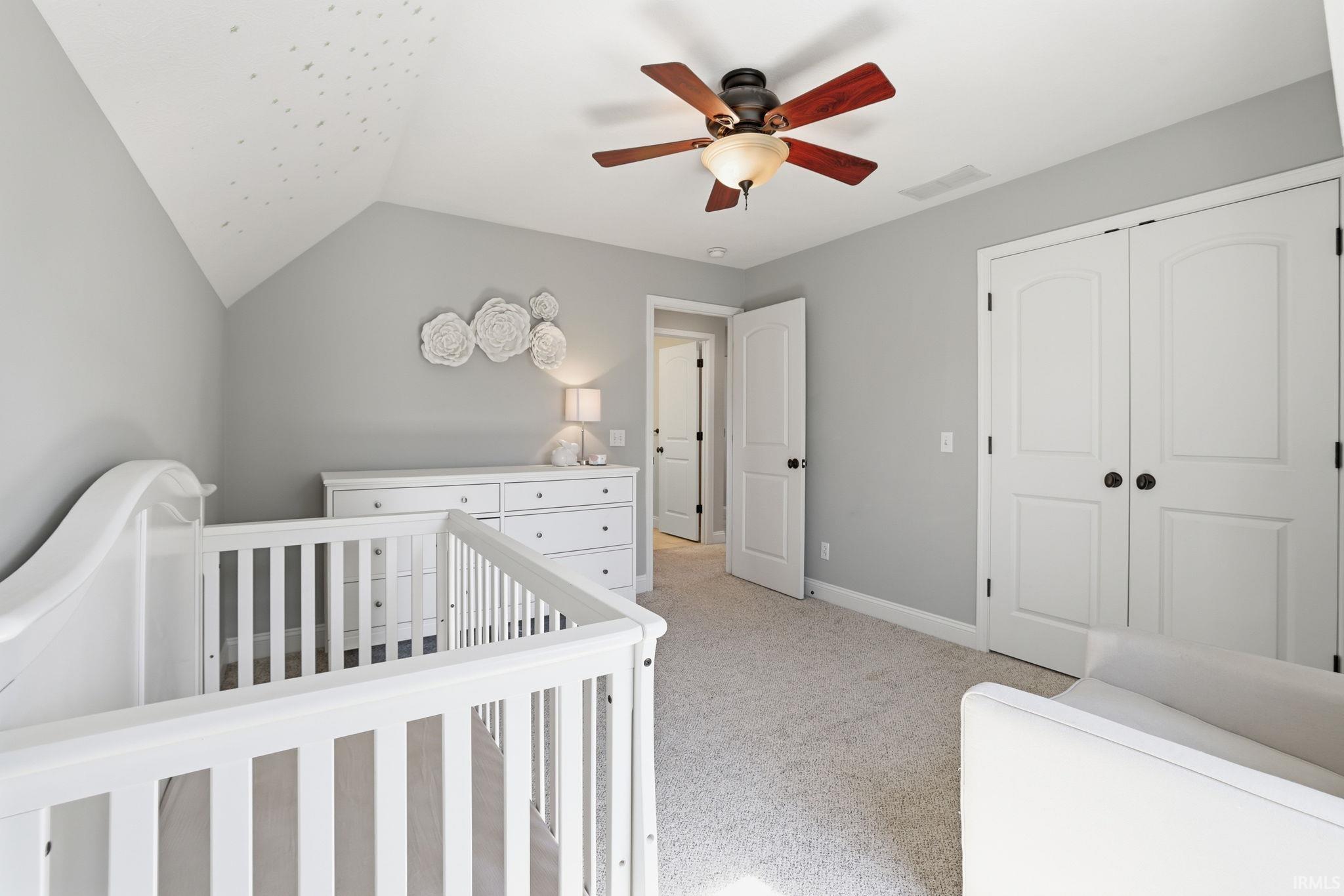 Nursery with a white crib, dresser, vaulted ceiling, and wood-blade ceiling fan.