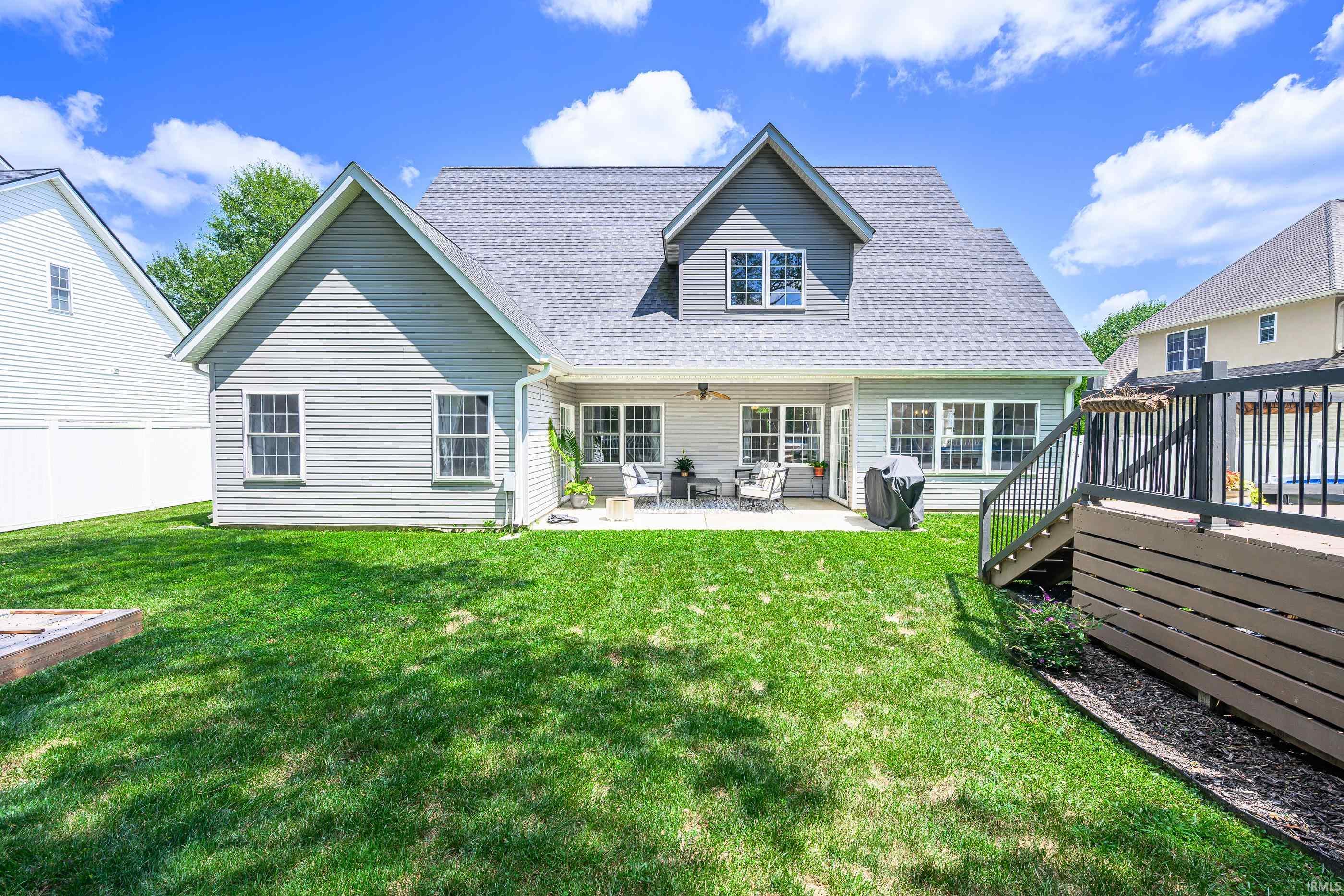 Rear of a gray house with a covered patio, broad lawn, and raised deck.