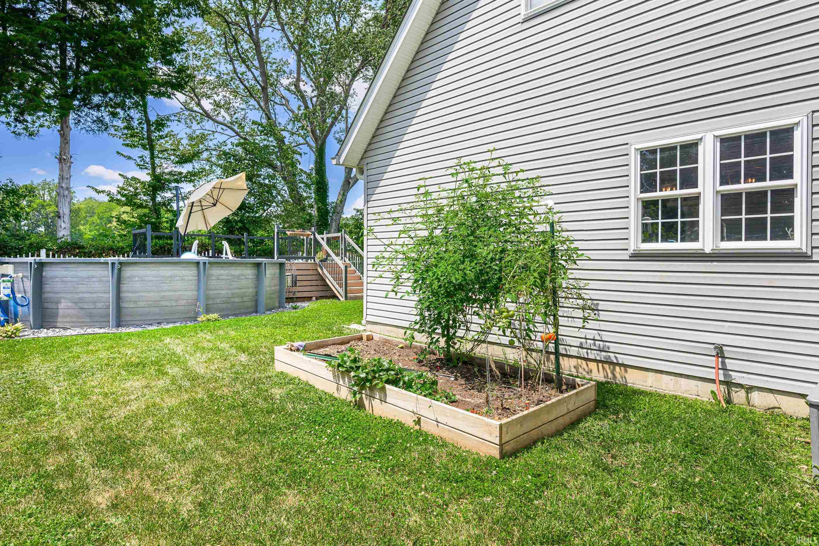 Backyard with a raised garden bed beside the house and an above-ground pool and deck.